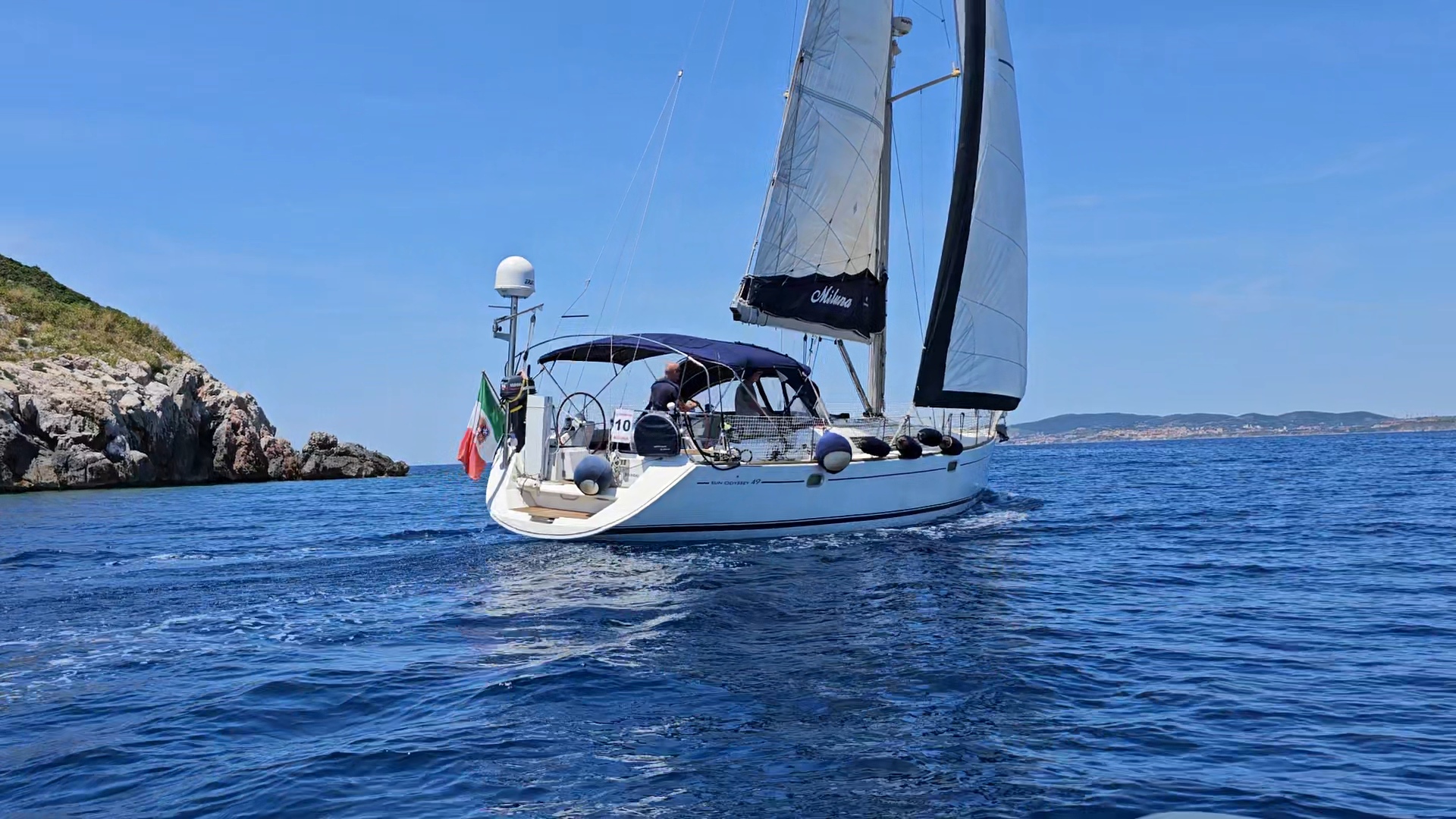 Sailing boat with Italian flag near rocky coastline